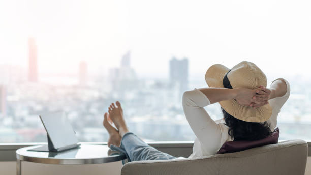 work-life-balance und lebensqualitätskonzept mit geschäftsfrau rückansicht entspannend in ruhe sitzen, es ruhig angehen im modernen hotelzimmer oder luxuriösen wohnzimmer mit schöner stadtszene - ausgewogenheit stock-fotos und bilder