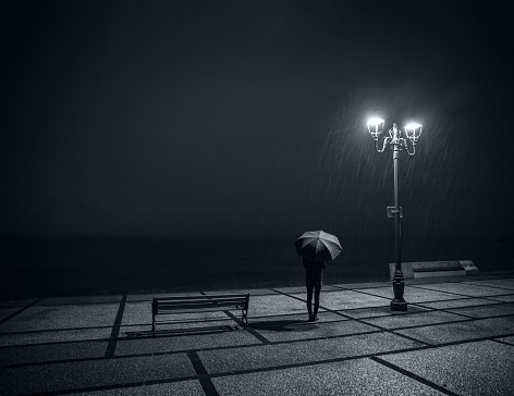 very beautiful view of a woman with an umbrella in the rain, at night, lit by a lamppost. Feeling of loneliness, sadness and melancholy
