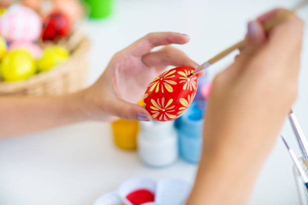 Close-up view of a person's hand in disposable gloves holding an Easter egg and coloring it in the colors of the Swedish national flag.