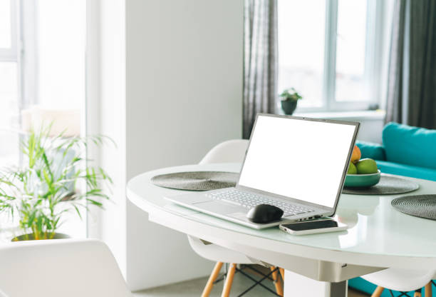 istock Open laptop with white screen on table on table in living room at home with bright interior, concept of remote working 1355927008