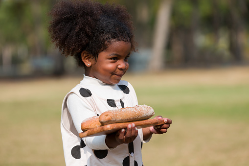 African American little girl holding bread while playing in the park
