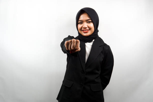 Beautiful young asian muslim business woman smiling confident, enthusiastic and cheerful with fists clenched at camera, punching, fighting, cooperation, eyes glinting, looking at camera isolated on white background stock photo
