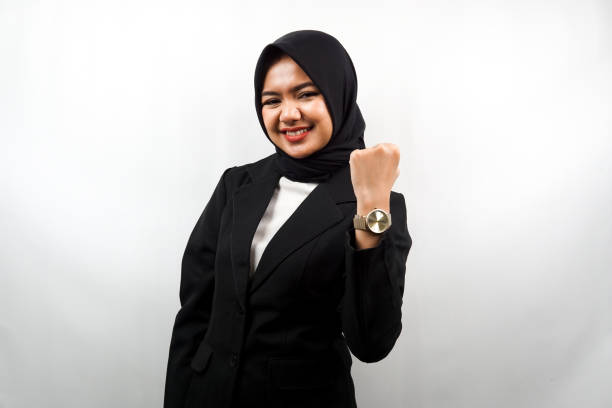 Beautiful young asian muslim business woman smiling confident, enthusiastic and cheerful with hands clenched, sign of success, punching, fighting, not afraid, victory, isolated on white background stock photo