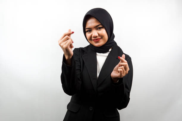 Beautiful young asian muslim business woman smiling, with korean love sign hand, hand close to camera, isolated on white background stock photo