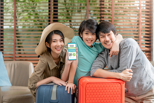 asian family ready to travel after covid lockdown is over,portrait of mother father and child boy son taking photo with luggage suitcase hand show smartphone  with vaccine passport application screen