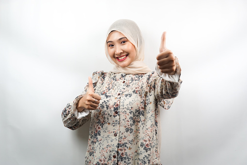Beautiful young asian muslim woman smiling confident, enthusiastic and cheerful with  hands thumbs up, ok sign, success, good job, success sign, isolated on white background