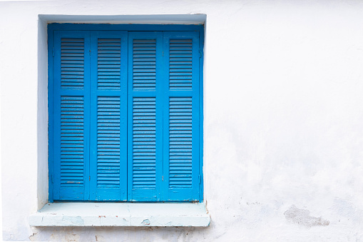 White painted wall with closed window, frame with blue shutter, space for text, lock down