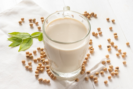 Soy or soya milk in a glass with soybeans backgroundSoy or soya milk in a glass with soybeans in wooden bowl background