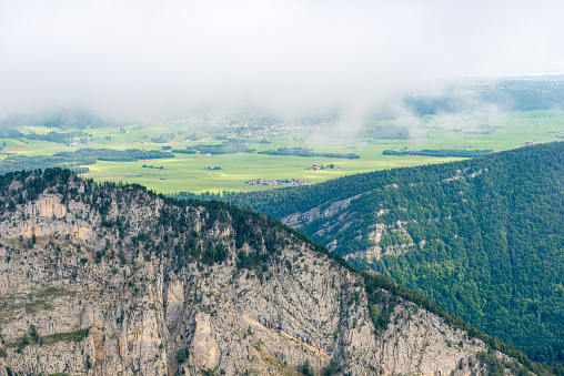 View of the barren and steep rock face, view of the barren and steep rock face, with a view of the green valley behind. Creux du Van is famous swiss canyon in the swiss jura mountains near Lake Neuchatel, between the cantons of Neuchâtel and Vaud, Switzerland.