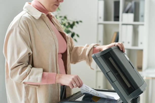 istock Close-up of office woman in beige shirt using scanner while making copy of document 1355954278
