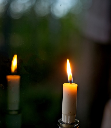 One candle with reflection on window. Peaceful warm feeling when candle gives weak but beautiful light to around it.