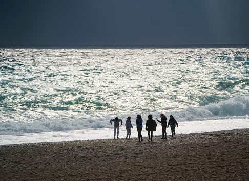 Antalya, Turkey - November 27, 2021: Group of teenage boys and girls playing with waves on the Konyaalti Beach, Antalya, Turkey