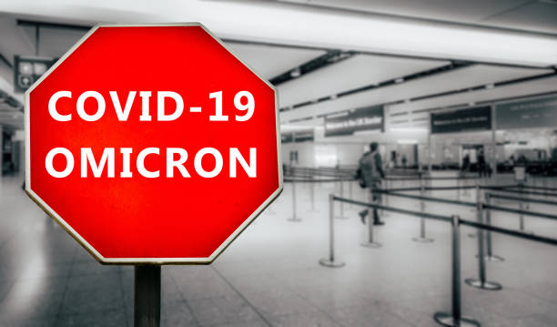Covid-19 Omicron written on stop sign with passengers arriving at passport control within generic airport stock photo