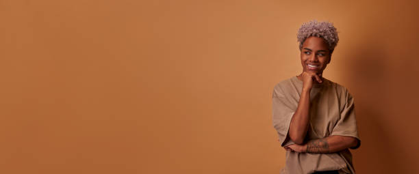 istock African female stands with broadly smile, keeps hands under chin over beige wall 1355961817