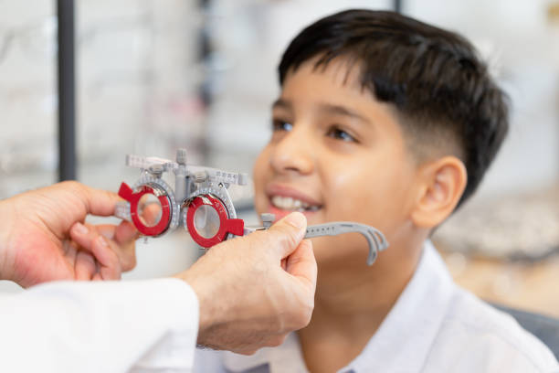 istock Selective focus at trial frame, Smiling Indian boy choosing glasses in optics store, Boy doing eye test checking examination with optometrist using trial frame in optical shop 1355962346