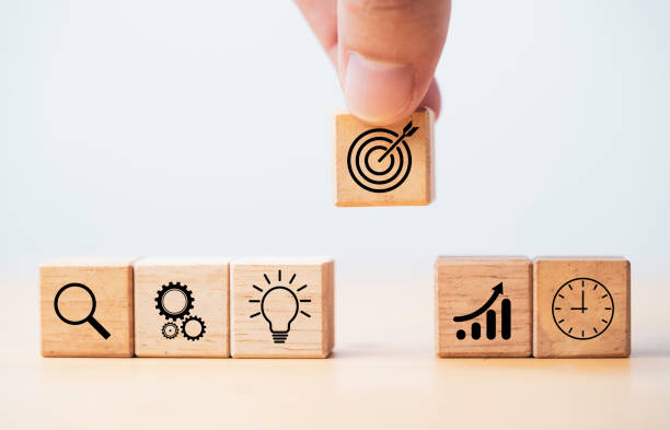 istock Hand  holding target board which printing on wooden cube block on mechanical gear and lightbulb icon  for creative and set up business objective target  goal concept. 1355963060