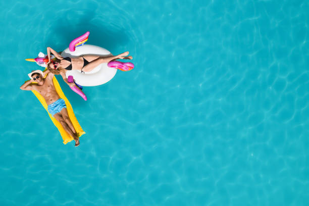 couple heureux avec anneau gonflable et matelas dans la piscine, vue de dessus. vacances - beach women swimwear summer photos et images de collection