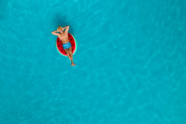 Happy man with inflatable ring in swimming pool, top view and space for text. Summer vacation