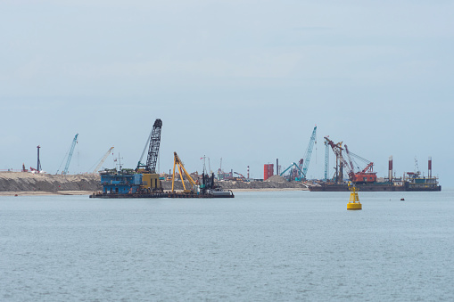 Construction machinery on barges performing land reclamation in the Johor Strait, off the coast of Tuas, Singapore.