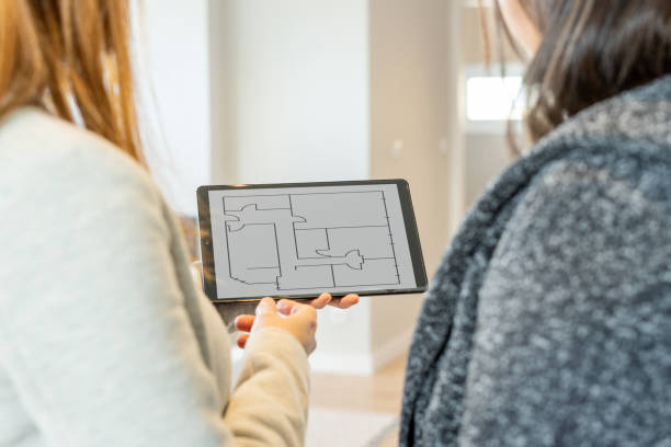Female real estate agent showing her client the plans of the property for sale through the tablet. Sale of property. stock photo