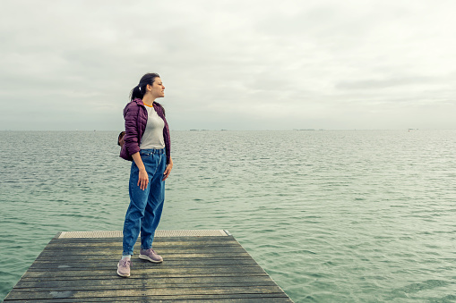 Woman with a backpack, looks at the sea, on a wooden pier. Freedom. Trips. Lifestyle.