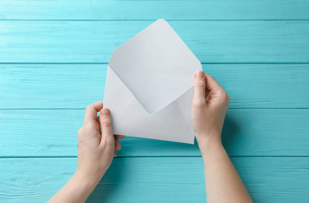 istock Woman with white paper envelope at light blue wooden table, top view 1355972172