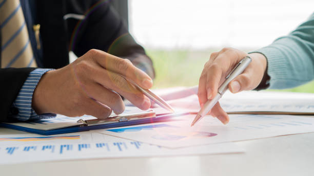 istock Business team discussing and planning projects using charts, holding pens and analytical papers on office table. with a laptop computer and a financial graph running in the background. business idea 1355972239