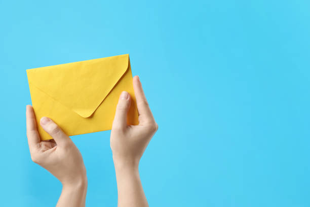 istock Woman holding yellow paper envelope on light blue background, closeup. Space for text 1355973849