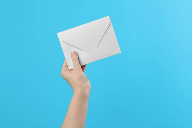 istock Woman holding white paper envelope on light blue background, closeup 1355973852