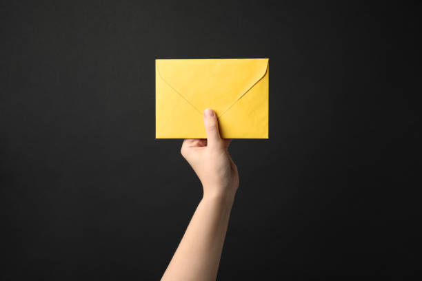 istock Woman holding yellow paper envelope on black background, closeup 1355974573