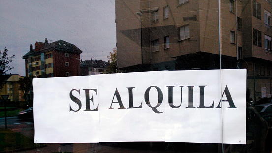 Renting sign on  window glass, text in spanish language. Apartment buildings reflected. Galicia, Spain.
