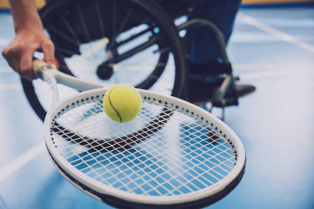 Adult man with a physical disability in a wheelchair playing tennis on indoor tennis court Adult man with a physical disability in a wheelchair playing tennis on indoor tennis court. wheelchair tennis stock pictures, royalty-free photos & images