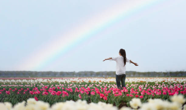 istock Female open arm in a rainbow flower field 1355982798