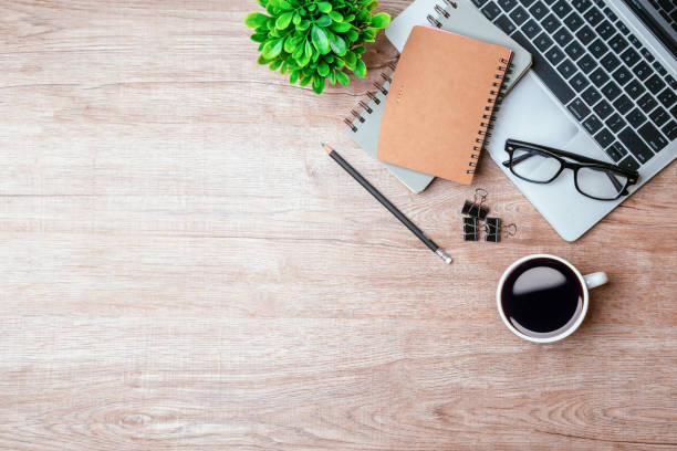 istock Work from home. desk office with laptop, blank notepad, coffee cup and pen on wood table. Flat lay top view copy spce. 1355985097