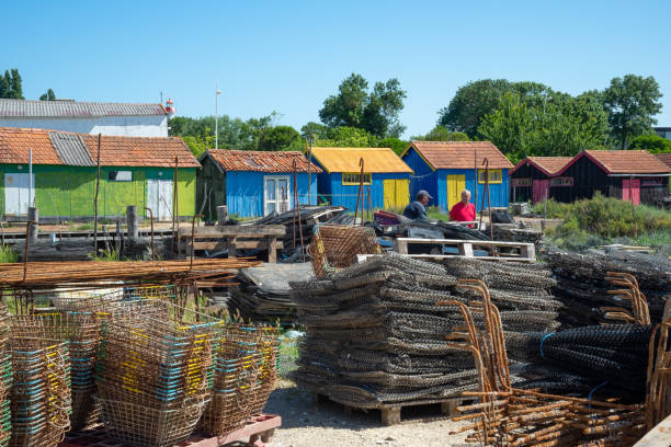 Two senior fishermen talking beside multi coloured oyster cabins and equipment at Chateau d’Oleron harbour famous oyster farming village and popular tourist travel destination on French Atlantic coast