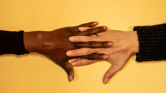 hands with fingers stretched and linked one of them is dark skinned and the other pale