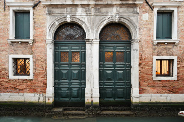 Two vintage green wooden doors and windows over canal in Venice, Italy