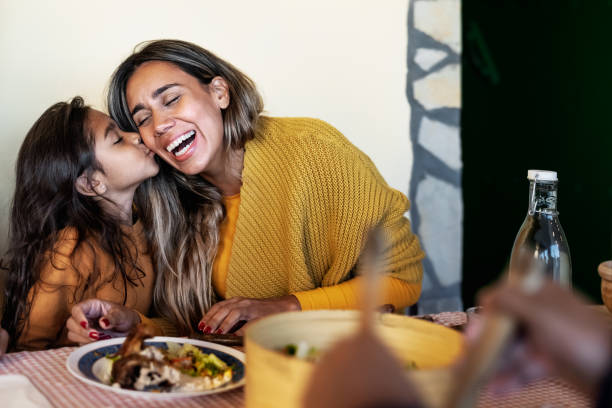 feliz madre hispana que tiene un momento tierno con su hija mientras cena junto con la familia - a los padres les encanta el concepto - restaurant food dinner lunch fotografías e imágenes de stock