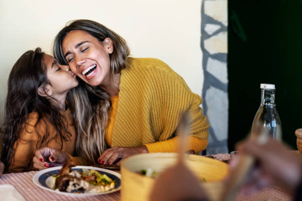 Happy Hispanic mother having tender moment with daughter while dining together with family - Parents love concept stock photo