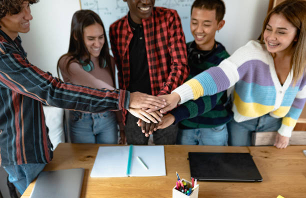 Young multiracial team of students putting their hands together while studying in classroom - Teamwork and unity concept stock photo
