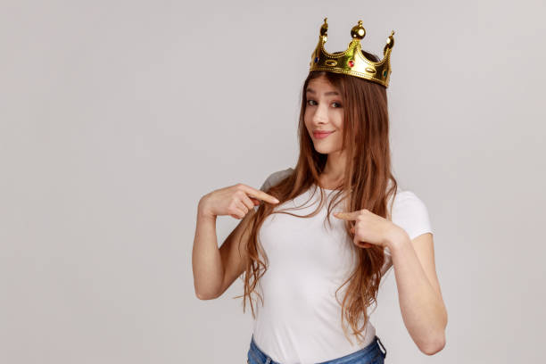 istock Woman with golden crown on head pointing herself and looking at camera, declaring her authority, 1356001265