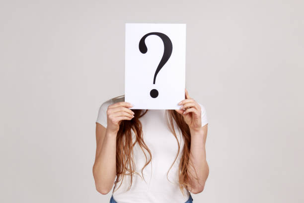 istock Anonymous woman hiding her face behind white paper with question mark, finding smart solution. 1356001273
