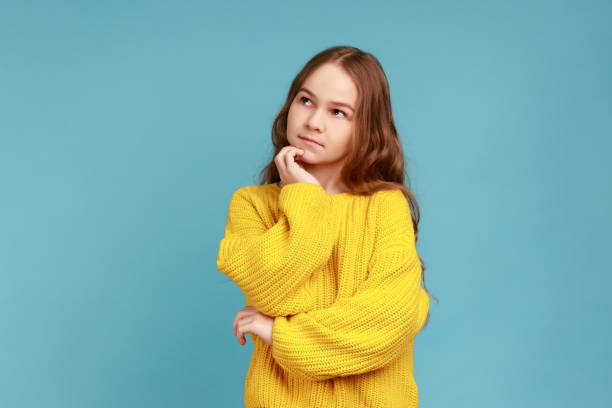 portrait of adorable thoughtful little girl stands holds chin, looking away with pensive expression. - pensive question mark teenager adversity imagens e fotografias de stock