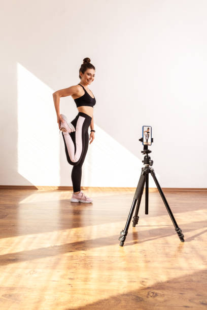 istock Athletic coach standing on one leg, stretching muscles before training, recording video for her vlog 1356001543