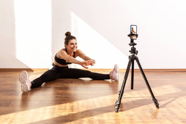 istock Female online trainer using phone on tripod for recording tutorials of stretching after workout. 1356001565