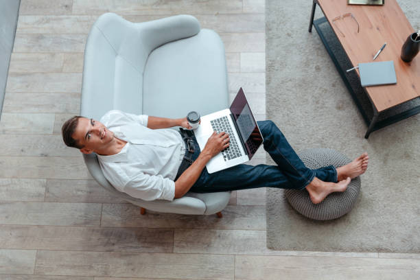 istock man with a Cup of coffee using a laptop while sitting on the sofa 1356001783