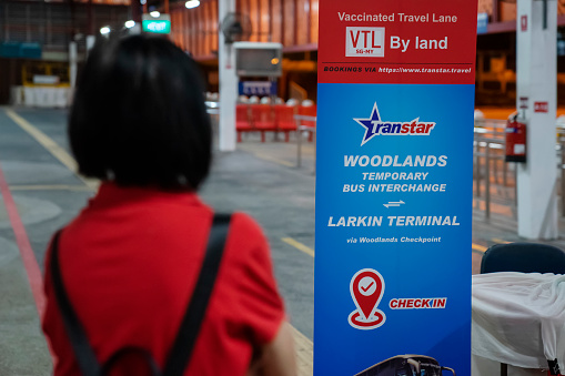 Singapore, Singapore - November 28, 2021: A woman looks at a banner indicating a check-in point for passengers boarding a bus heading from Woodlands to Malaysia, as part of a vaccinated travel lane (VTL) agreement. Singapore and Malaysia begin a VTL from November 29.