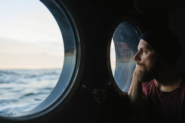 uomo alla finestra dell'oblò di una nave che naviga nell'oceano - nave di passeggero foto e immagini stock