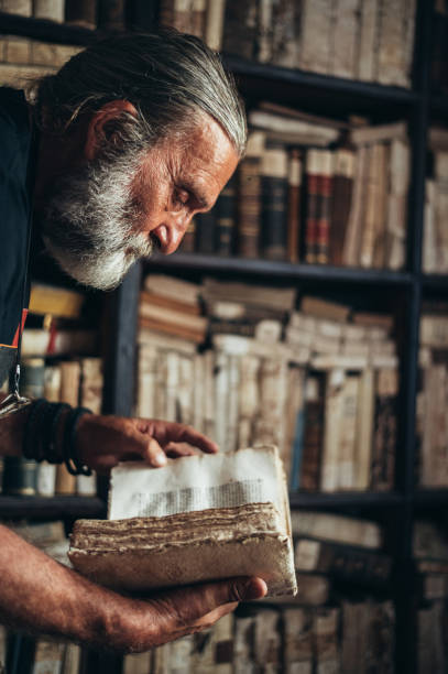 istock Senior man hands holding an old book in a library 1356010096