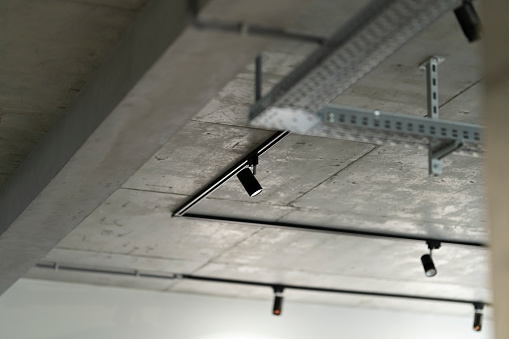 Loft interior style fragment. Black track lights on a concrete ceiling. Led track spotlights and corrugated wiring on the ceiling.